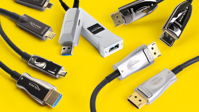 Verschiedene schwarze und silberne Delock-Kabel und -Adapter (USB-C, USB-A, HDMI, DisplayPort) verstreut auf leuchtend gelbem Hintergrund.